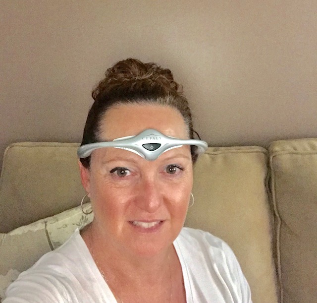 a woman sitting on a couch with a CEFALY device on her forehead